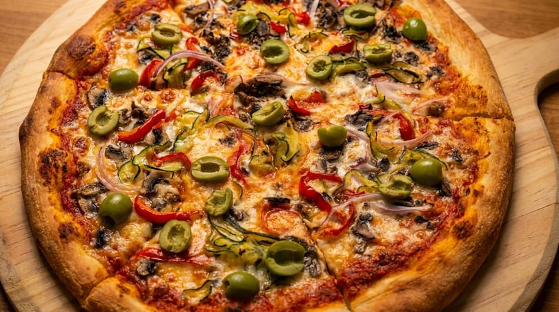 A freshly baked vegetarian pizza with olives, mushrooms, peppers, and onions on a wooden board.