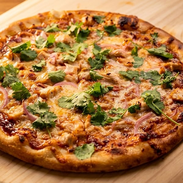 BBQ chicken pizza with red onions and cilantro on a wooden pizza peel.