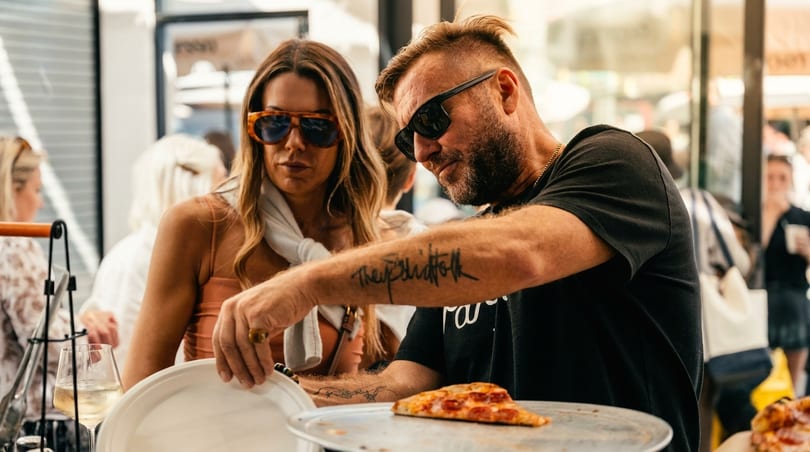 A man serves a slice of pepperoni pizza to a woman at an outdoor event.