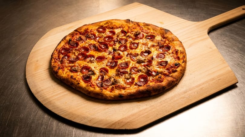 Freshly baked pepperoni and sausage pizza on a wooden pizza peel, ready to serve.