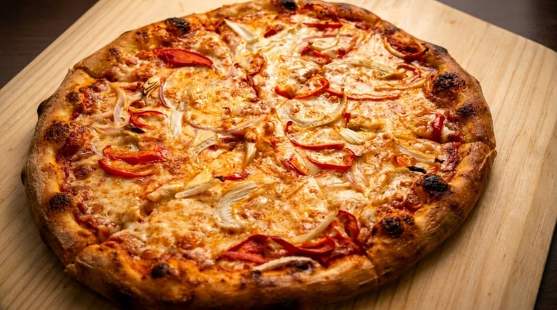 A freshly baked pizza with melted cheese, red peppers, and onions on a wooden board.