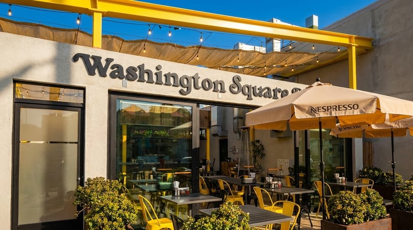 Washington Square restaurant exterior with outdoor seating, yellow chairs, and Nespresso umbrellas under a blue sky.